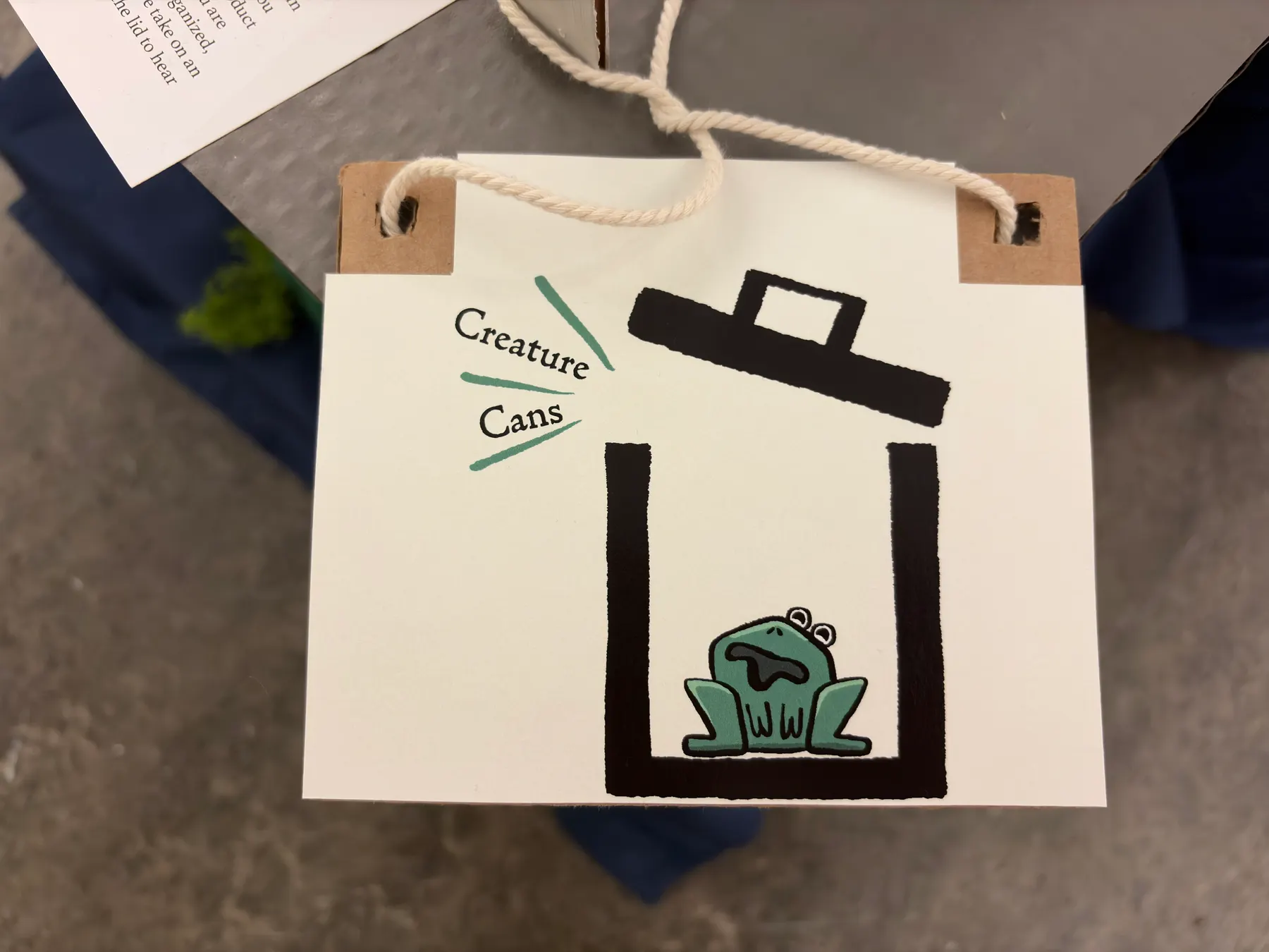 The frog trash can from the front showing the googly eyes and painted green body.